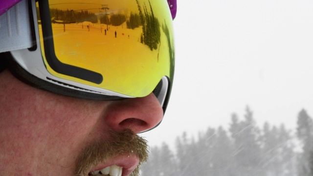 滑雪者滑下滑雪道的慢动作镜头在一个男性滑雪板的护目镜的反射在一个阴天的冬天在滑雪斜坡视频下载