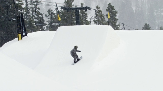 完成一个“前侧360 Tucknee”技巧与森林和滑雪缆车在背景在科罗拉多州博尔德附近的埃尔多拉滑雪度假村在一个下雪的，阴天从远处视频素材