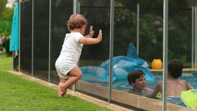宝宝靠在泳池围栏上想和泳池里的孩子们互动的可爱瞬间视频素材
