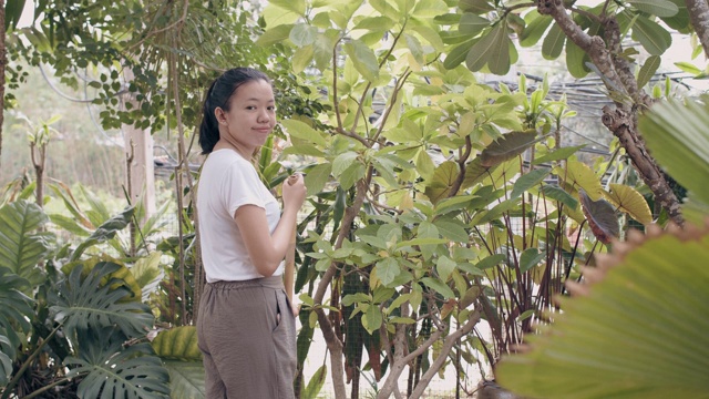 亚洲妇女在后院花园用扫帚扫干树叶家。4 k慢动作。视频素材