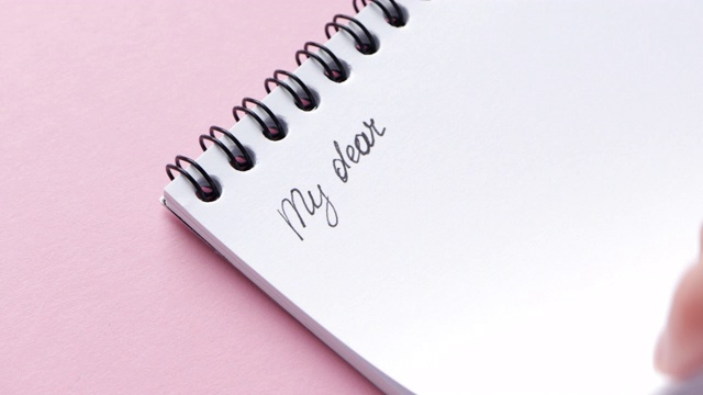 删除纸记事本与手写的字在粉红色的背景，特写视频素材