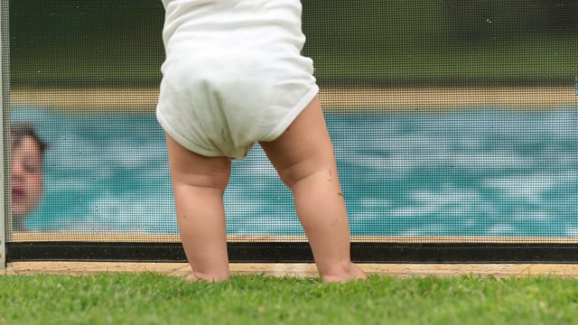 夏天的时候，婴儿倚在泳池围栏上看着孩子们在泳池水里玩耍视频素材