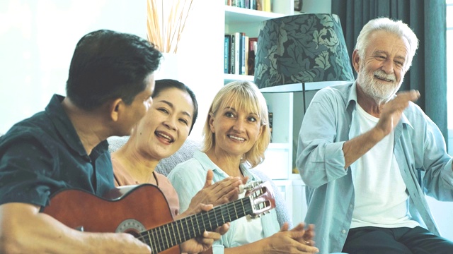 一群老年人在客厅里玩吉他开派对。白人，亚洲人，泰国人坐在家里的沙发上。退休生活方式的概念。边拍摄。视频素材
