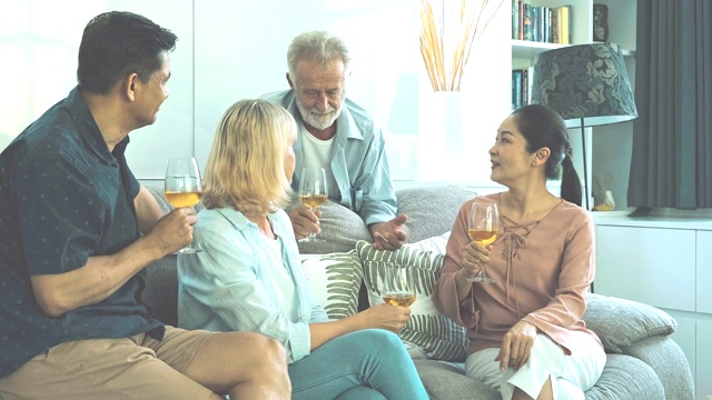 一个老人在客厅里喝着白葡萄酒和朋友聊天。白人，亚洲人，泰国人坐在家里的沙发上。退休生活方式的概念。视频素材