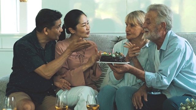 一群老年人在客厅举行生日聚会鼓掌。白人，亚洲人，泰国人坐在家里的沙发上。退休生活方式的概念。视频下载