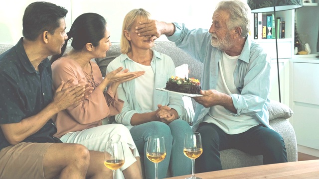 老人在客厅的生日聚会上给妻子一个惊喜。白人，亚洲人，泰国人坐在家里的沙发上。退休生活方式的概念。视频素材