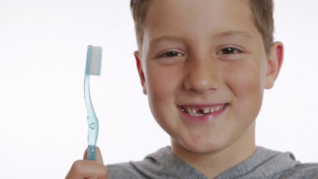 特写肖像快乐微笑的男孩拿着牙刷。没有门牙的快乐男孩。视频下载