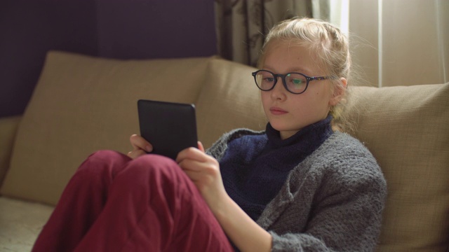 9岁女孩在家沙发上看电子书视频素材