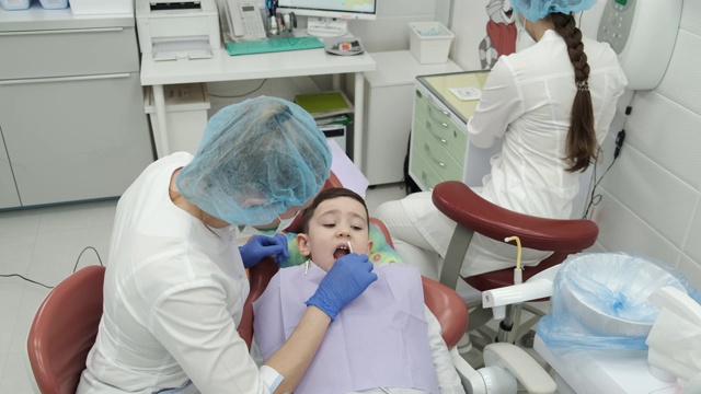 男孩在牙医的预约、健康检查、刷牙准备、口腔治疗、消毒、张口、牙医、室内、医生的办公室、牙科椅、预防、医用口罩、防护视频素材