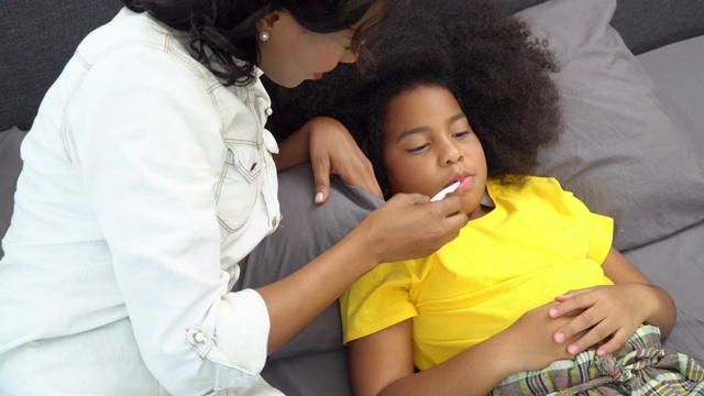 4K非洲裔美国母亲用手和数字口腔温度计检查她生病的女儿的温度。可爱的小女孩躺在床上患了感冒和流感。母亲和保健概念。视频素材