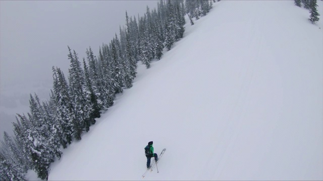 在冬季暴风雪中，男人爬着陡峭的雪坡视频下载