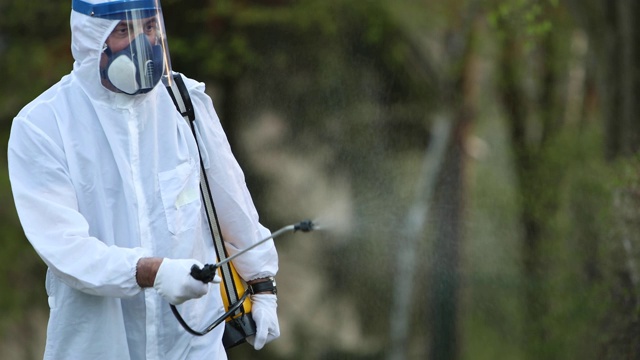 一个穿着传染病防护服的人对空旷的暴露区域进行消毒的录像视频下载