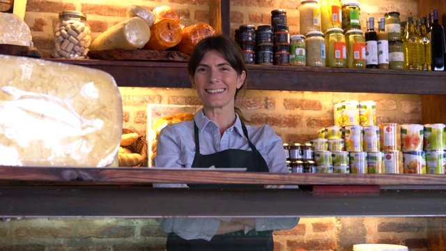 自信开朗的女老板在一个熟食店站在冰箱后面对着镜头微笑视频下载