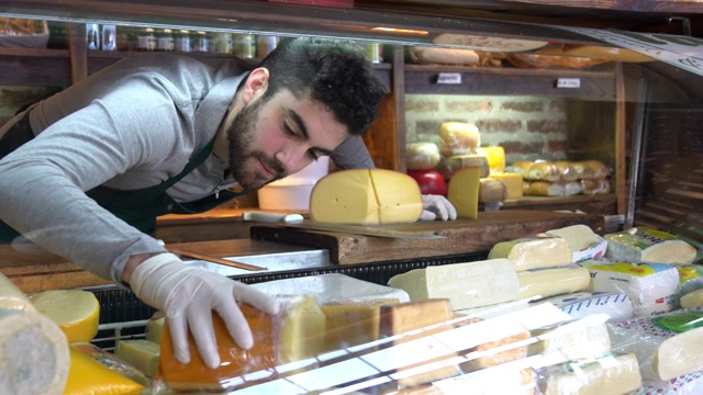 年轻的拉丁美洲男子安排奶酪冰箱展示在熟食店视频下载