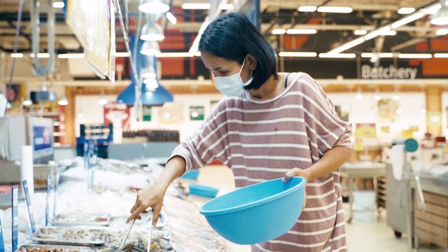 年轻的亚洲女性选择在超市商店冷冻虾和鱼海鲜，并戴上面罩以预防冠状病毒或新冠肺炎和流感，以保持健康。视频素材