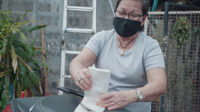 年长的亚洲妇女戴着口罩，同时准备一个袋子。视频素材
