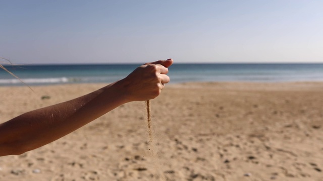 从一个往海滩上撒沙子的女孩手中。时间在你指缝间流逝。女孩抱着一沙一海的背景。手里拿着沙子。假期和海边之旅的概念视频素材