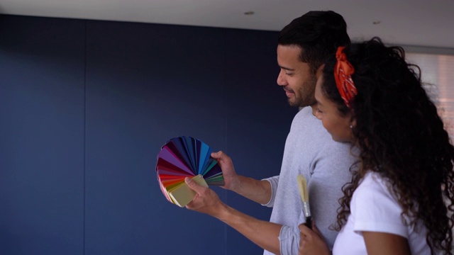 一对快乐的夫妇看着一块色块和他们想在新家粉刷的墙视频下载