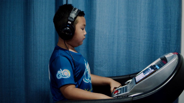 慢动作亚洲男孩戴着耳机在跑步机上行走视频素材