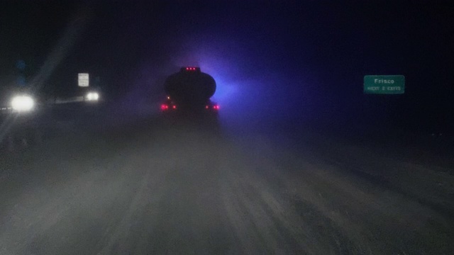 车辆视点拍摄在暴风雪中，在繁忙的道路上驾驶在一辆油罐车的后面，而前方的应急灯在夜晚闪烁视频素材
