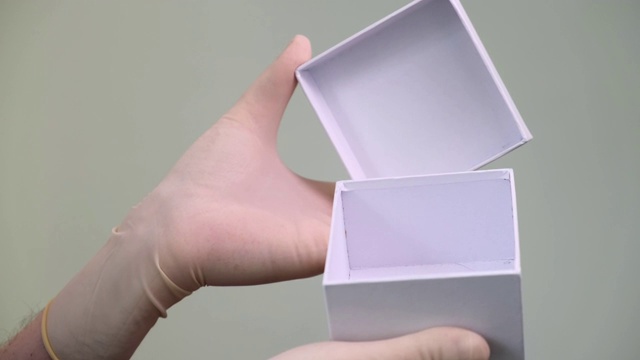 男性双手在防护乳胶手套给予和打开空的白色礼盒。视频下载