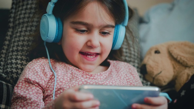 小女孩在玩手机游戏。开心地玩手机游戏。她用耳机来避免被打扰。一个5岁的小女孩在玩手机游戏。学龄前儿童在小工具上玩游戏。视频素材