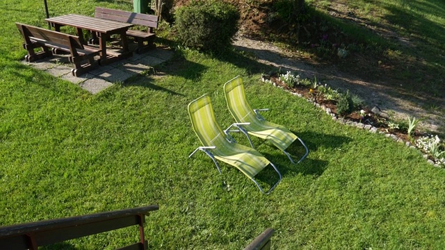 花园中绿色草坪上的金属折叠躺椅和木桌和长凳。一个漂亮整洁的花园，有休闲区和餐厅。视频素材