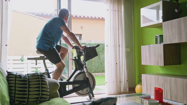 后方视频视图的成熟男子在锻炼自行车在家视频素材