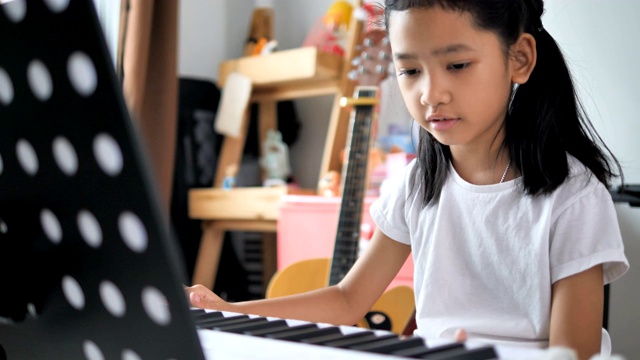 亚洲小女孩学习弹奏基本钢琴使用电子合成器键盘初学者音乐器乐自学在家视频素材