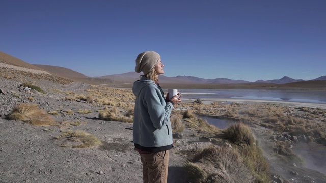 一个女人站在安第斯山脉中一个冒着热气的湖边喝茶视频下载