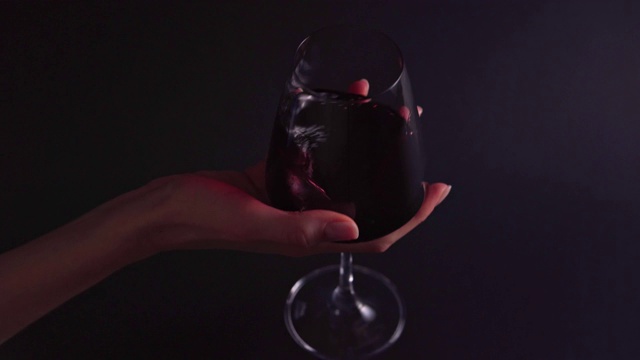 葡萄酒的味道——一个女人的手在黑色背景上旋转着一个杯子。酒吧或餐厅的专业人士品尝4k酒精饮料视频下载