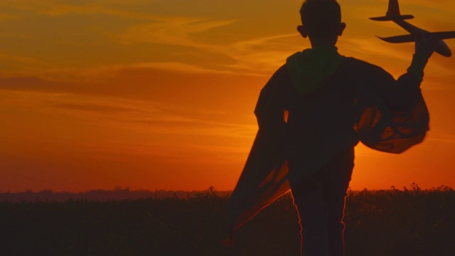 一个男孩正在田野上跑，手里拿着一架飞机。日落。4 k视频素材