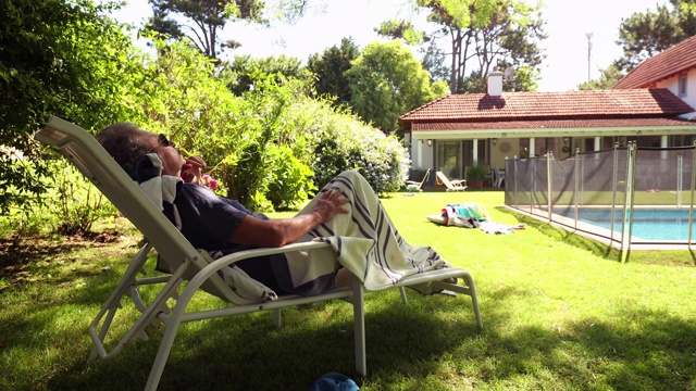 一个沉思的老人在后院休息。一位退休老人躺在泳池边视频素材