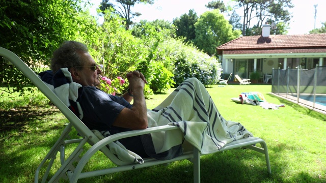 年长的男人在家里的后院花园放松。退休男子躺着休息视频素材