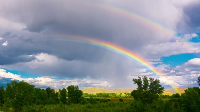 明亮的彩虹从绿色草地上的云下降时间间隔4k视频下载
