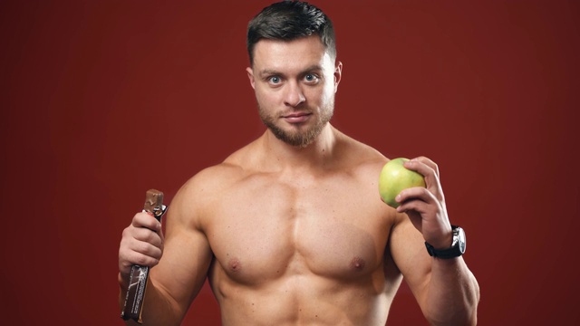 一个运动员在新鲜苹果和巧克力之间选择的肖像。视频下载