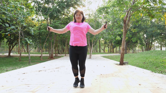 亚裔白种人胖女孩漂亮的脸穿着粉红色的运动服，早上在公园里通过跳绳锻炼，保健用运动减肥视频下载