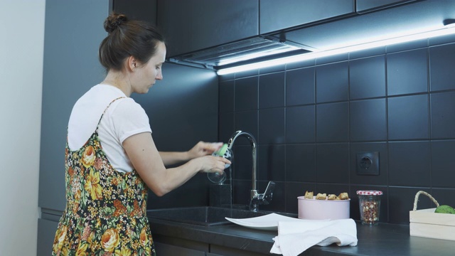 女人用海绵和清洁剂在厨房水槽里洗玻璃。女人打扫厨房。家庭主妇用自来水在厨房水槽里洗盘子。打扫屋子的概念视频下载