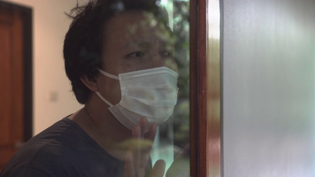 亚洲男子通过窗口自我隔离检查冠状病毒或Covid-19视频素材