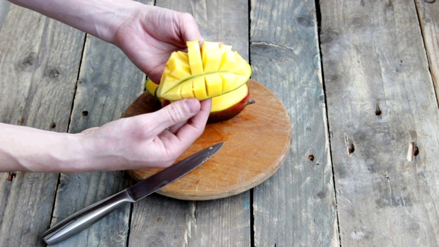 男人的手把芒果切成半块，放在木头的背景上视频下载