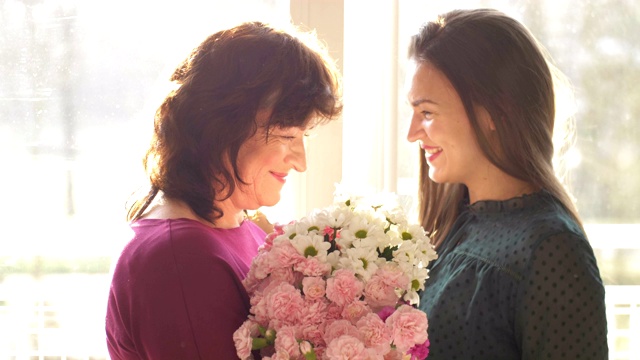 年轻的成年女子女儿拥抱快乐的中年母亲，拥抱亲情，用母亲节的概念祝贺成熟的母亲，献上鲜花，一起庆祝视频下载