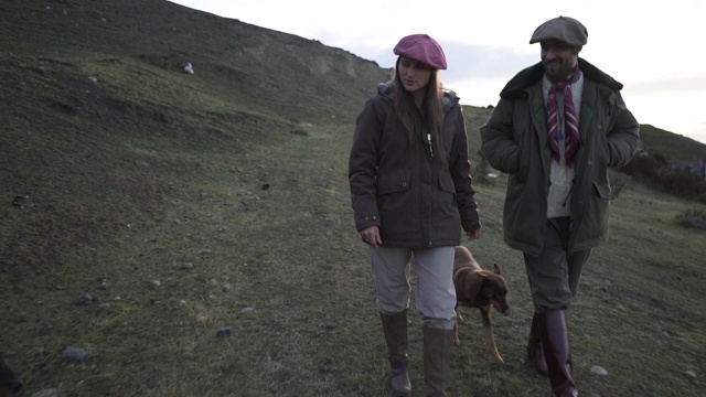 近距离的年轻夫妇牧羊场主坐在他们的狗在草原日落视频素材