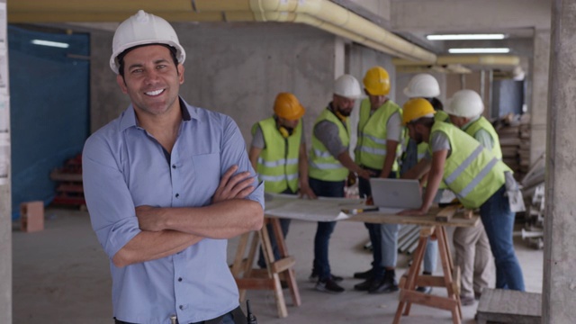 英俊的建筑监理在一个建筑工地微笑与双臂交叉的镜头视频素材