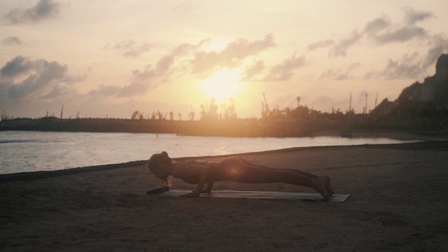 日出时，女孩在垫子上做上下犬式瑜伽视频下载