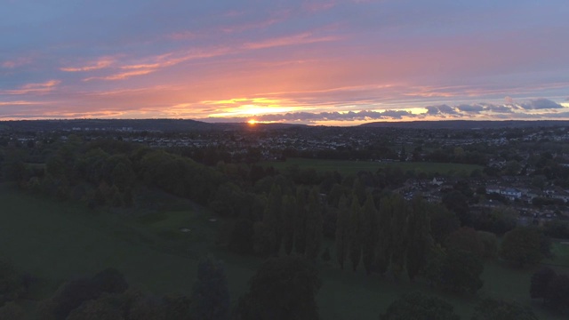 从树后升起的日落航拍展现了绿色的乡村，英国郊区的房屋和南布里斯托尔彩色天空的夕阳视频下载