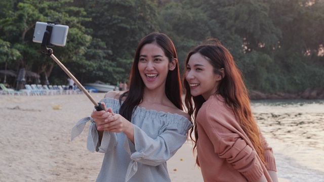 美丽的亚洲女人和朋友使用智能手机在海滩合影。视频素材