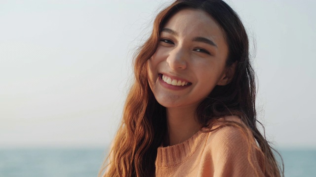 美丽的年轻女子的肖像看着镜头与迷人的微笑在海的背景。视频素材