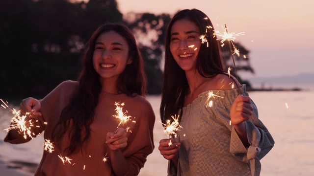 美丽的年轻女子和她的朋友玩火花舞蹈在海滩与海洋的背景。视频素材