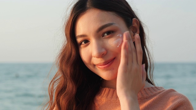 一名快乐的年轻亚洲女性在海滩度假期间正在涂抹护肤霜来护理她的皮肤。视频素材