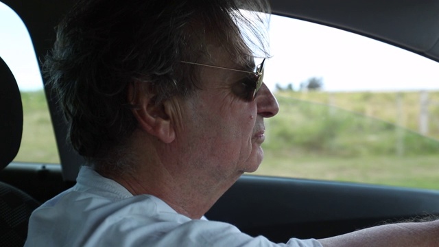 在乡村路上开车的老人。放松、沉思、休闲的高级男子司机在路上戴着墨镜视频下载